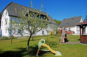 Un quartier résidentiel avec une maison blanche, un arbre dans la cour et une structure de jeux pour enfants.