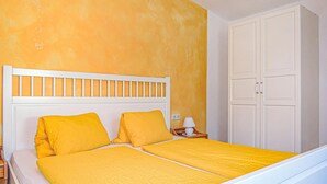 Un llit amb capçalera blanca i roba de llit groga en una habitació amb paret groga i un armari blanc.