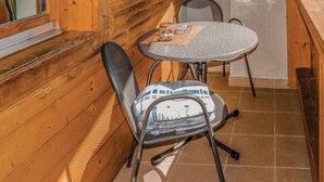 Interior d'una cabana de fusta amb una taula rodona i dues cadires, una d'elles amb coixí estampat.