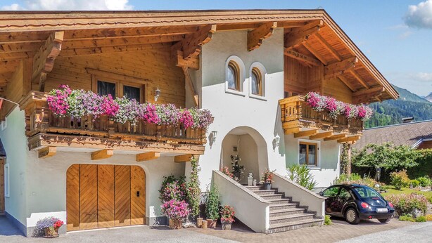 Una xalet de fusta tradicional amb un balcó decorat amb flors, una escala de fusta i un cotxe a la façana.