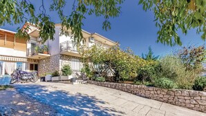 Un edificio residencial de varios pisos con fachada de piedra, un balcón y un camino de entrada pavimentado.