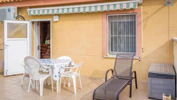 Une terrasse extérieure avec une table et des chaises, une fenêtre ornée de barreaux décoratifs et une petite poubelle.