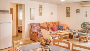Een gezellige woonkamer met een bank, stoelen, een eettafel en een keuken met een koelkast.