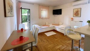 Una habitación pequeña y acogedora con una cama, un escritorio y una silla. Cuenta con una ventana con cortinas, un televisor de pantalla plana en la pared y una mesita con un tapete rojo.