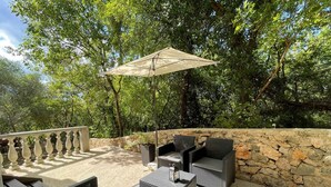 Un patio al aire libre con muebles de mimbre, un muro de piedra y vistas a exuberante vegetación.