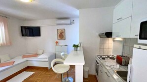 Una cocina compacta con estufa a gas, microondas y gabinetes blancos. Hay un pequeño comedor con una mesa blanca y dos taburetes de bar.