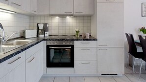 A modern kitchen with white cabinets, a built-in oven, a coffee maker, and a dining area with a table and chairs.
