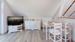 A room with a TV, white furniture, a dining table, and a view of the outdoors.