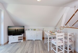 A room with a TV, white furniture, a dining table, and a view of the outdoors.