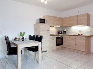 A modern kitchen with light wood cabinets, a dining table with chairs, a microwave, a coffee maker, and an oven.