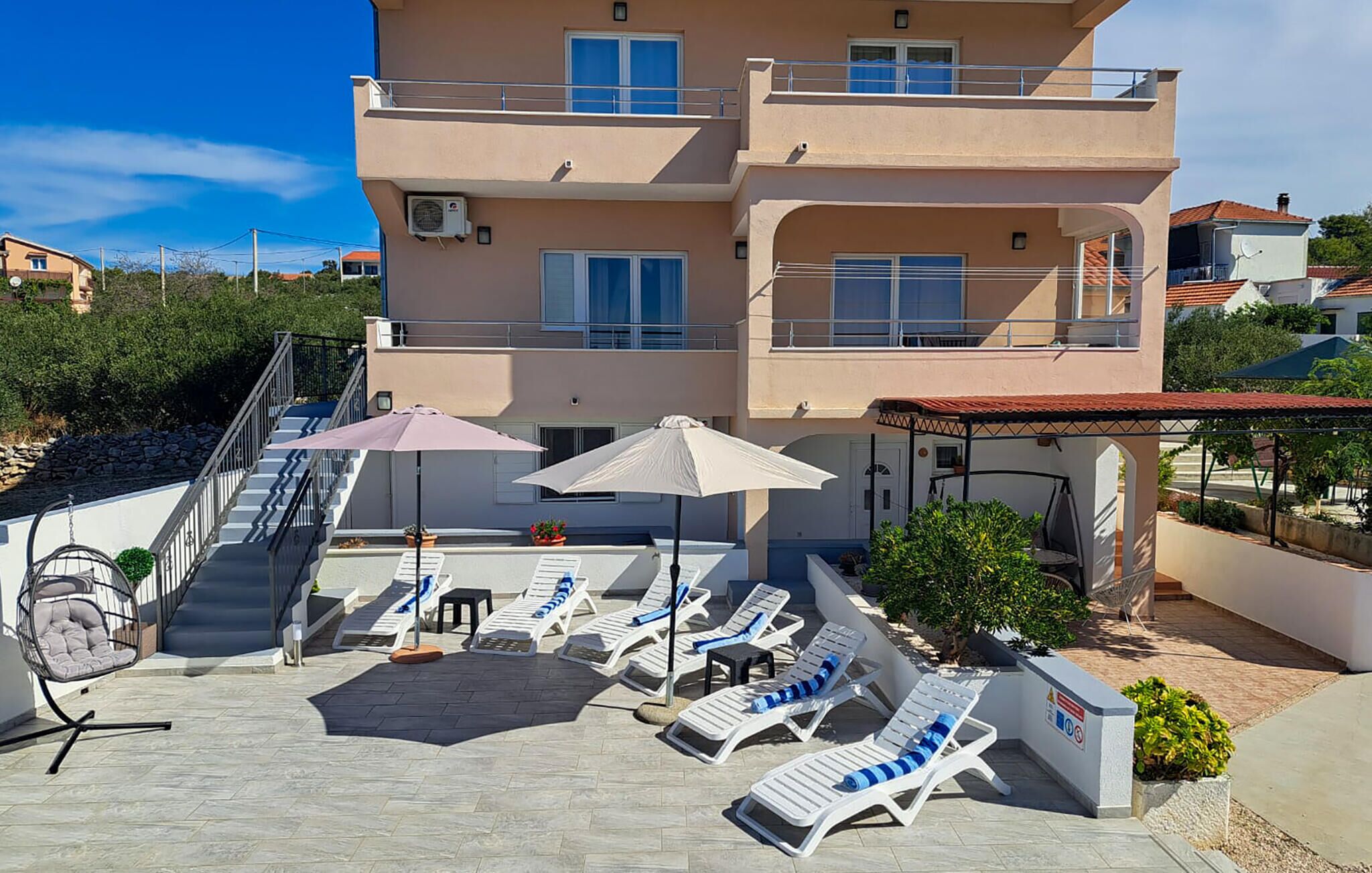 Un immeuble à plusieurs étages doté d’un espace piscine comprenant des chaises longues et des parasols, d’un escalier et d’un espace salon abrité.