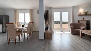 Een moderne woonkamer met een eethoek, een bank, een aan de muur bevestigde televisie en een balkon met uitzicht.