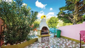 Un patio con suelo de mosaico, un horno exterior amarillo y blanco, y abundante vegetación.