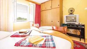 Una habitación con cama, televisión, armario de madera y ventana con cortinas.
