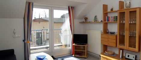 Una sala de estar con televisor, una mesa de comedor con sillas, una estantería y una ventana con cortinas.