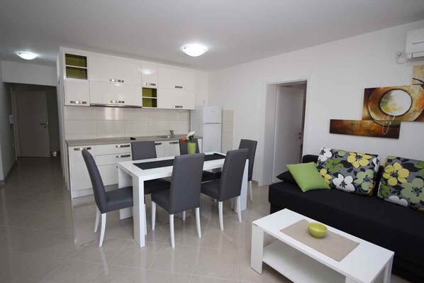 A modern kitchen with white cabinets, a dining table with chairs, and a black sofa with floral cushions.