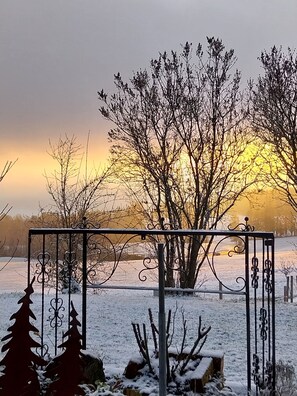 A metal gate with intricate designs, a snow-covered landscape, and leafless trees against a sunset. - FW Haflinger - Hof Roßruck (Fischbachau)