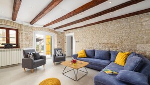Un salón espacioso con una pared de piedra, un sofá azul con cojines amarillos, una mesa de centro de madera y un reposapiés amarillo.