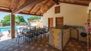 Un espacio al aire libre cubierto con piscina, mesa de comedor, sillas y una zona de cocina con lavadora.
