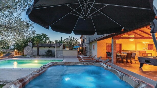 Un área de piscina con hidromasaje, sillas de descanso y una sombrilla.