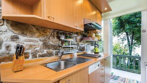 Une cuisine avec des meubles en bois, un mur en pierre, un évier en acier inoxydable et une fenêtre donnant sur un espace verdoyant.