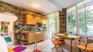 Une cuisine chaleureuse avec des murs en pierre, des armoires en bois et un coin repas comprenant une table et des chaises.