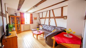 Un salon chaleureux avec un plancher en bois, un canap é en cuir, un meuble en bois et une table rouge ornée de fleurs.