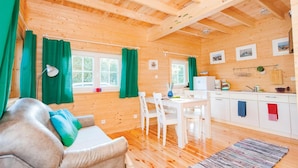 Un intérieur de chalet chaleureux avec un canapé, une table à manger, des chaises et un coin cuisine.