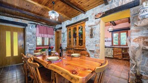 A rustic dining area with a wooden table and chairs, stone walls, and a kitchen visible in the background. - Beautiful home in Nedescina (Nedescina)