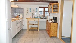 Una cucina con mobili bianchi, un tavolo di legno, una macchina per caffè e una sveglia appesa al muro.