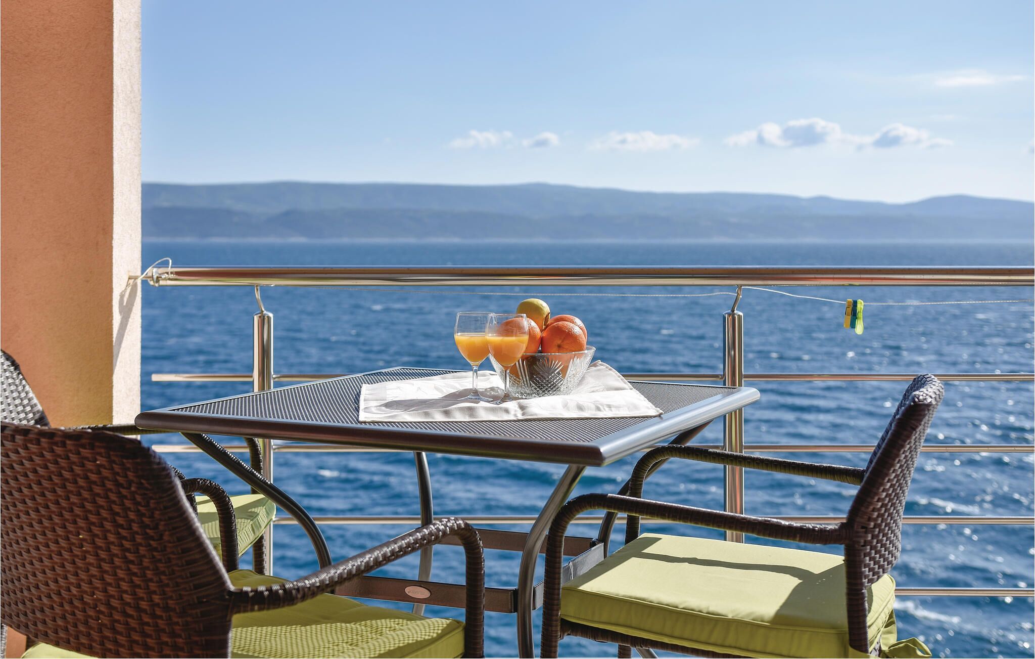 Ein Tisch mit Orangensaft, Obstschale und Speisekarte auf einem Balkon mit Blick auf das Meer.
