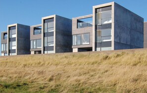 Ein modernes Gebäude mit flachem Dach und großen Fenstern, gelegen auf einem grasbewachsenen Hügel.