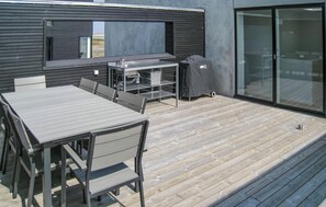 Eine moderne Außenpatio mit Holzboden, einem Metallgrill und einer Glasschiebetür.