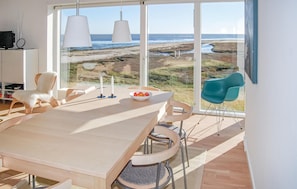 Ein moderner Essbereich mit großem Tisch, Stühlen und Blick auf Strand und Meer durch große Fenster.