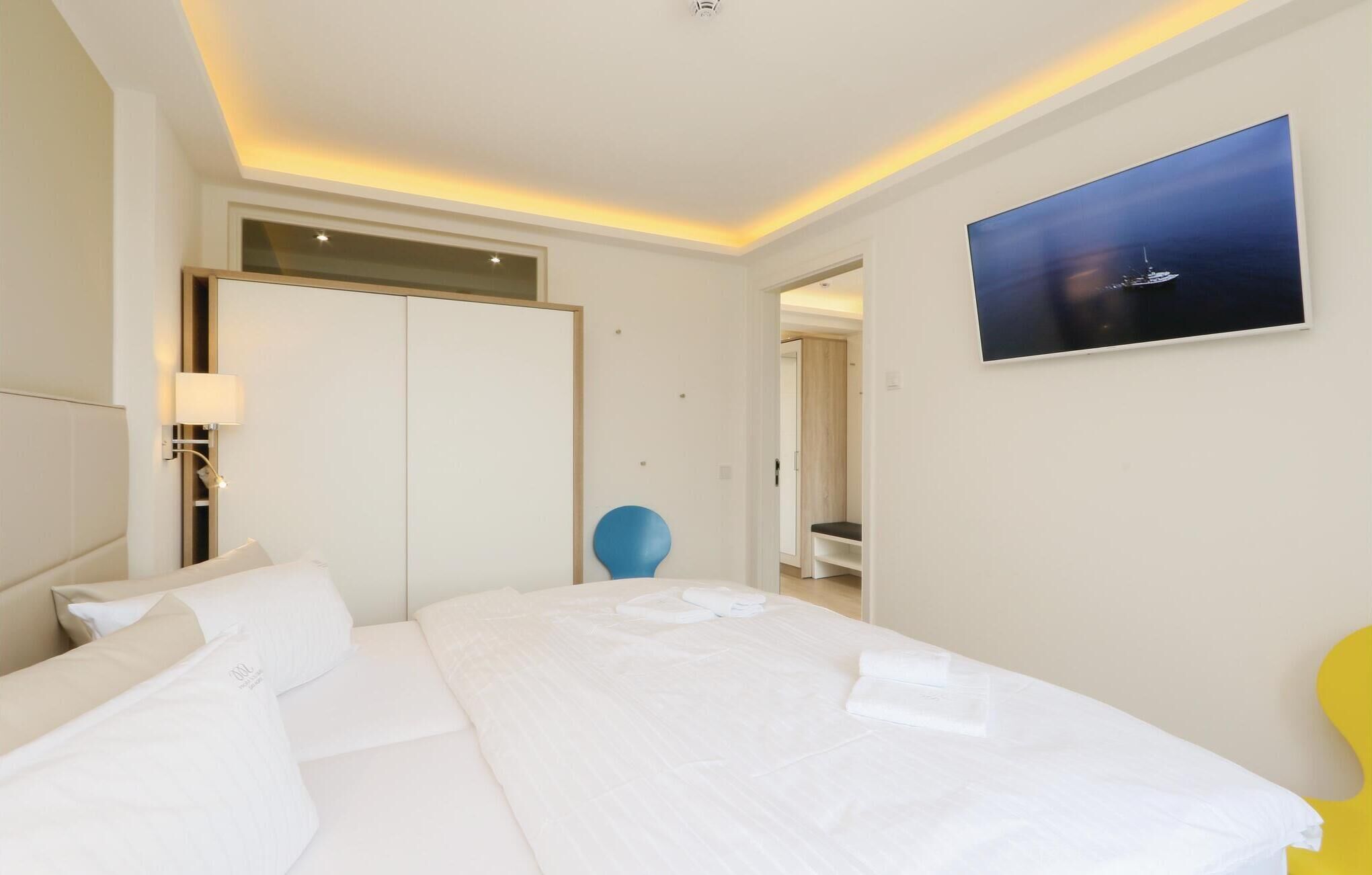 A hotel room with a large bed, a desk, a chair, a wardrobe, a painting, and a bathroom visible through an open door.