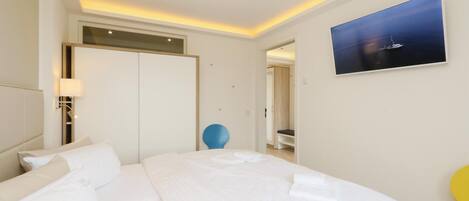 A hotel room with a large bed, a desk, a chair, a wardrobe, a painting, and a bathroom visible through an open door.