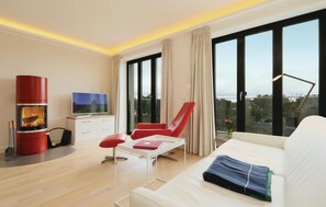 A modern living room with a sofa, red chair, TV, and a fireplace. - Beach front apartment in Binz with indoor swimming pool (Prora/Rügen)