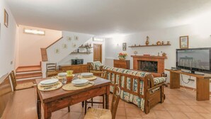 A spacious living room with a fireplace, a dining area with a wooden table and chairs, and a television on a stand. - Beautiful home in Gavorrano GR with WiFi (Gavorrano GR)