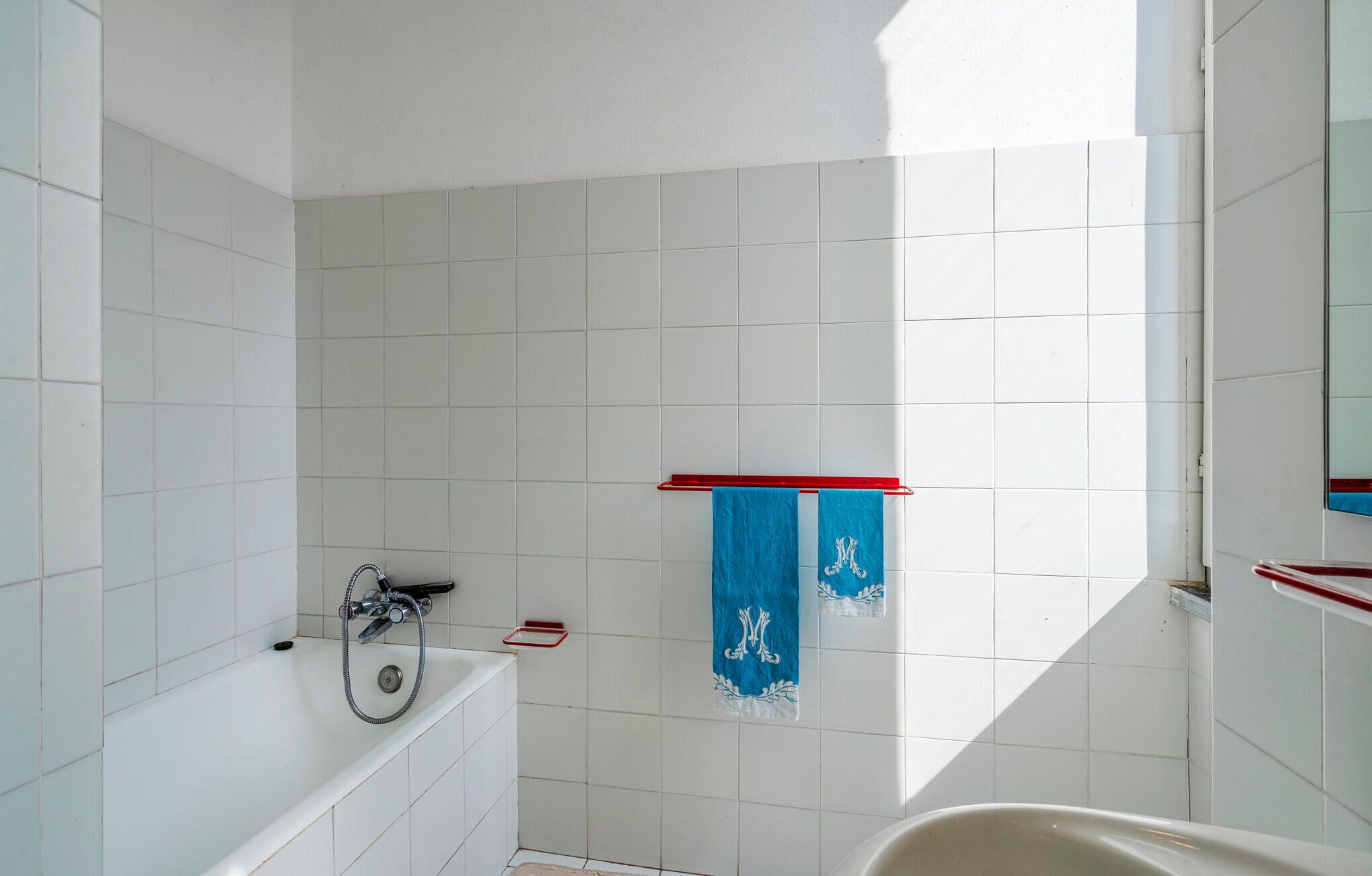 A bathroom with white tiled walls, a bathtub, and a shower. There are two towels hanging on a rack.