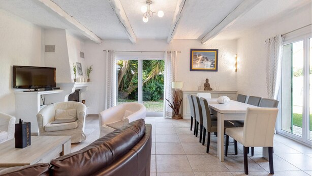 A spacious living room with a brown leather sofa, a white armchair, a television, and a dining area with a table and chairs. - Lovely home in Sainte Maxime (Sainte Maxime)