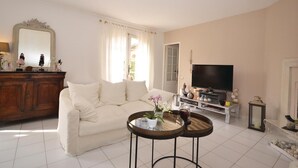 Ein Wohnzimmer mit einem beigen Sofa, einem Holzschrank, einem Fernseher und zwei kleinen runden Tischen.