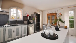 Eine Küche mit Herd, Spüle und Schränken. Ein Fenster mit Vorhängen und eine Uhr an der Wand sind ebenfalls vorhanden.