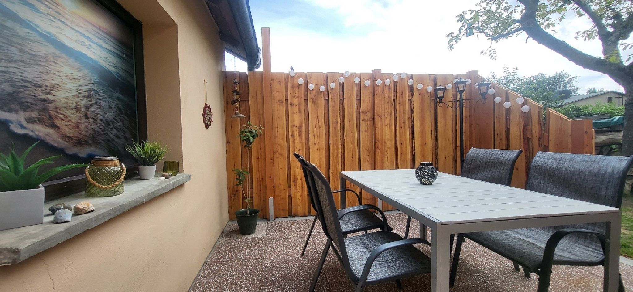 A patio with a table and chairs, a wooden fence, and potted plants.