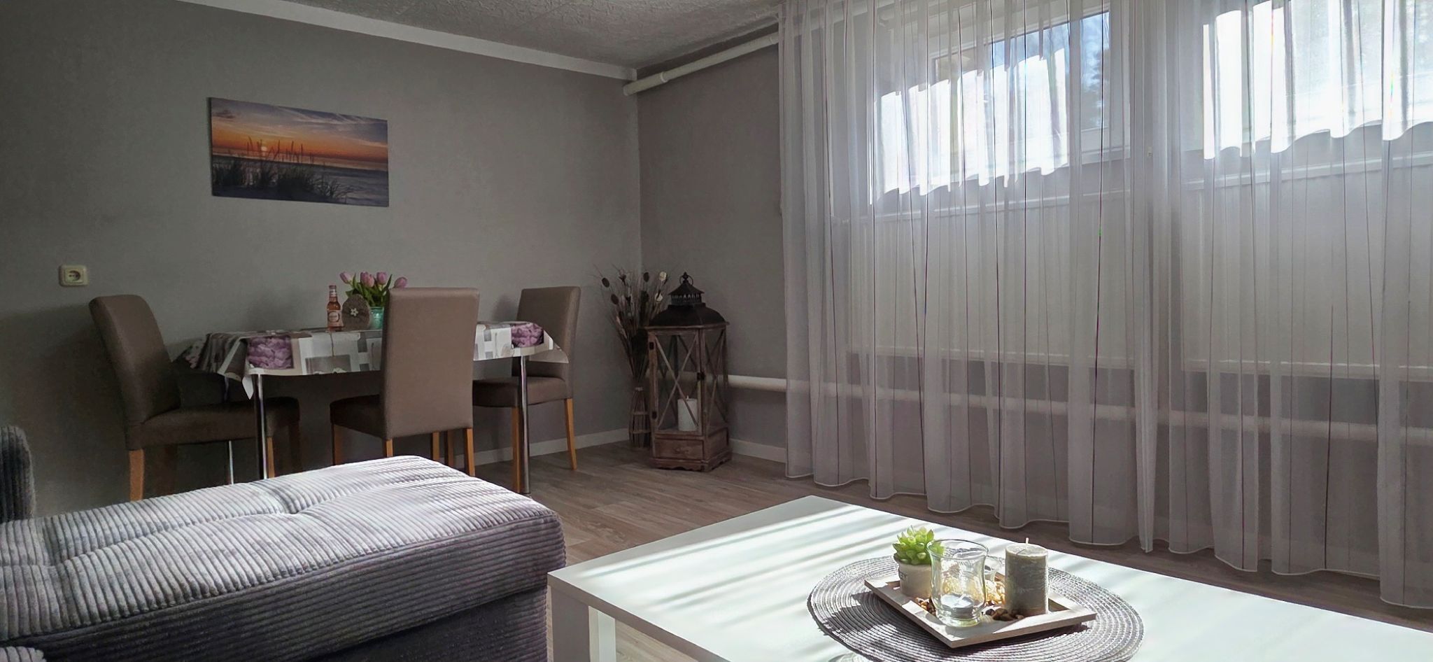 Ein Wohnzimmer mit Essbereich, einer Couch, einem Tisch mit Dekoration und transparenten Vorhängen.