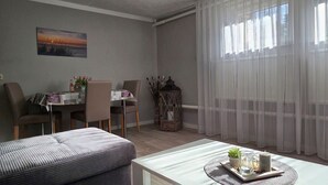 A living room with a dining area, a sofa, a table with decorative items, and sheer curtains.