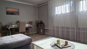 Ein Wohnzimmer mit Essbereich, einer Couch, einem Tisch mit Dekoration und transparenten Vorhängen.