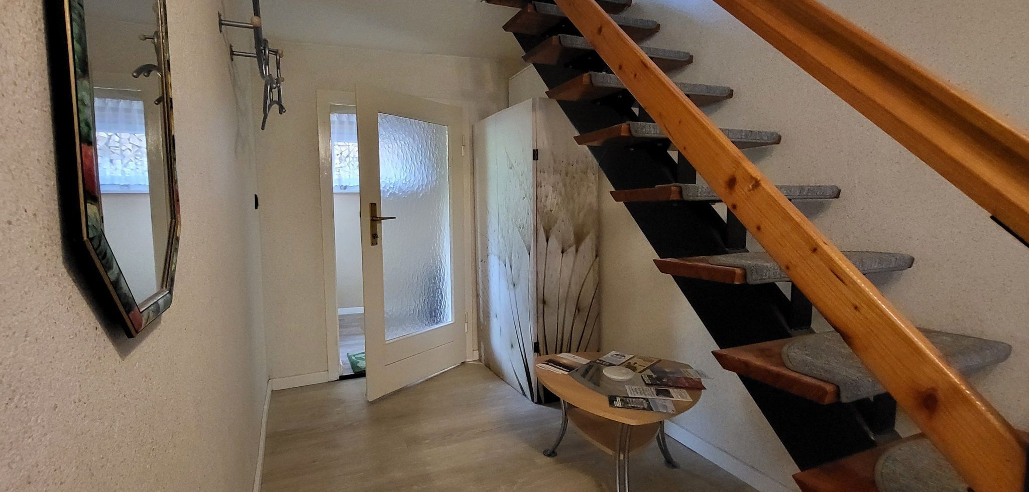 Eine Treppe führt zu einer zweiten Etage, ein Spiegel an der Wand und ein kleiner Tisch mit Papieren.