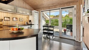 A modern kitchen with a wooden ceiling, a large island with a fruit bowl, and a sliding glass door leading to an outdoor patio.