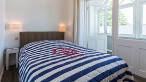 Ein Zimmer mit einem Bett, zwei Nachttischlampen, einem Vorhangfenster und Blick auf Grünfläche.