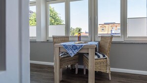 Ein Zimmer mit Tisch und Stühlen, großen Fenstern und Blick auf Gebäude.